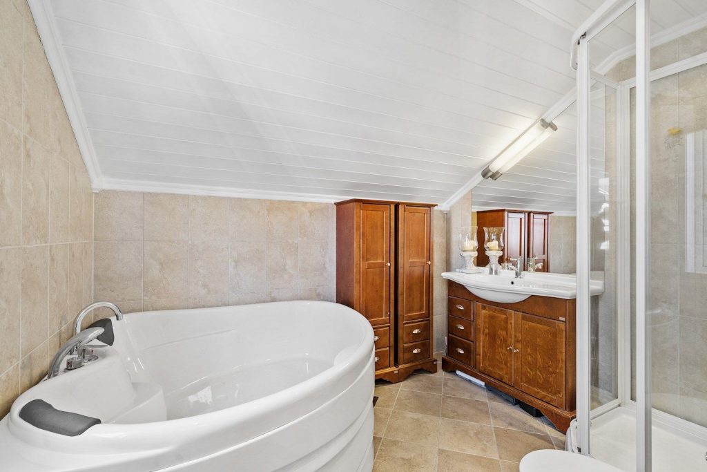 Farmhouse bathroom in old style with shower, corner bath tub and stylish wooden bathroom interior. 